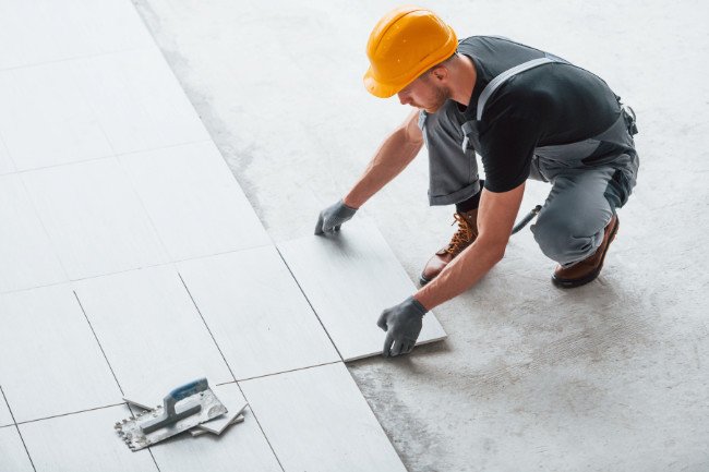 Installation of plates. Man in grey uniform and orange hard hat works indoors in modern big office at daytime Installation of plate. Man in grey uniform and orange hard hat works indoors in modern big office at daytime.